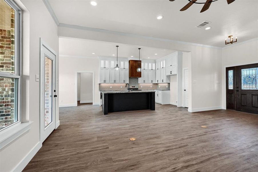 Kitchen featuring backsplash, wood-type flooring, an island with sink, ceiling fan, and hanging light fixtures