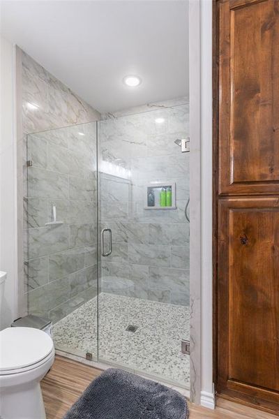 Glass-enclosed shower featuring marble-look tile walls, pebble flooring, and a recessed niche Glass-enclosed shower featuring marble-look tile walls, pebble flooring, and a recessed niche