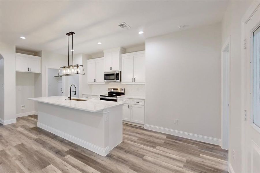 Kitchen with white cabinetry, appliances with stainless steel finishes, sink, and a kitchen island with sink