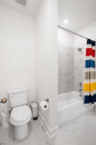 A well-lit bathroom showcases sleek white tiled flooring and a convenient shower-tub combination.