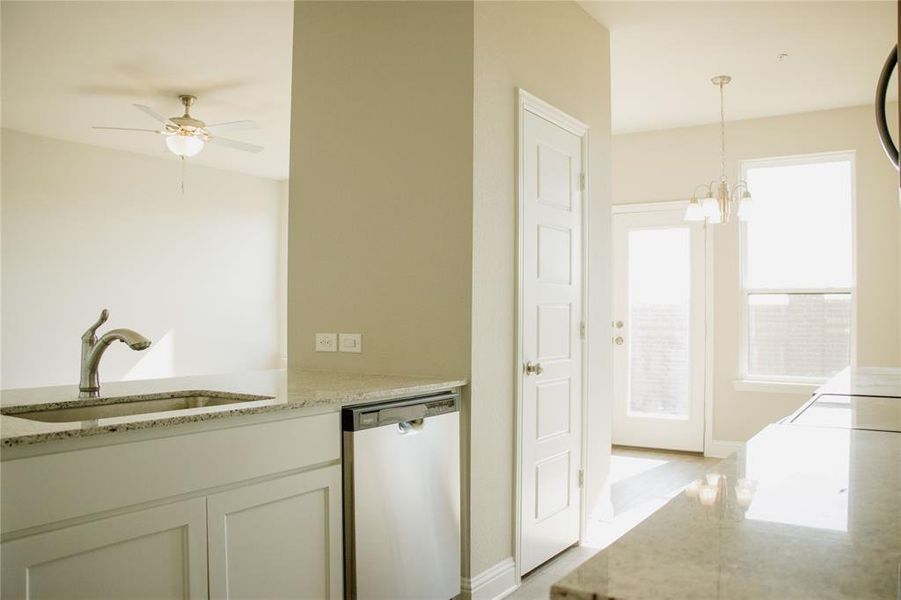 Kitchen featuring light stone countertops, sink, stainless steel dishwasher, pendant lighting, and ceiling fan with notable chandelier