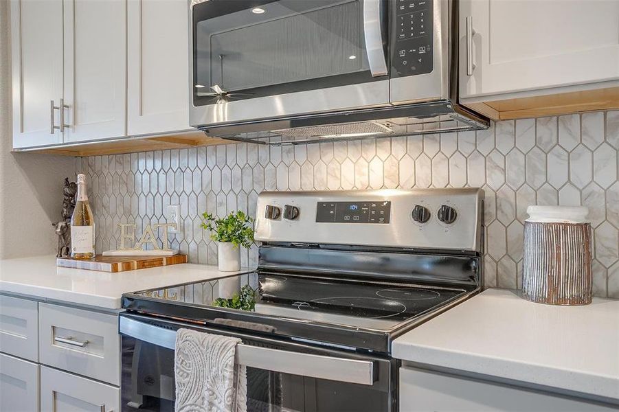 Kitchen featuring appliances with stainless steel finishes, backsplash, and white cabinetry