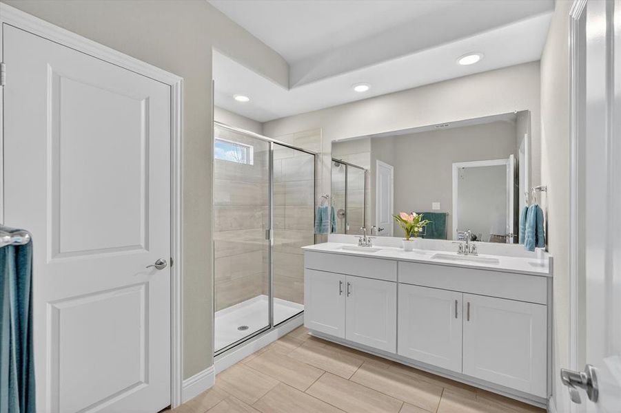 Bathroom featuring a dual vanity with white cabinetry and integrated sinks, a large frameless mirror, and a glass-enclosed shower with tile surround Bathroom featuring a dual vanity with white cabinetry and integrated sinks, a large frameless mirror, and a glass-enclosed shower with tile surround
