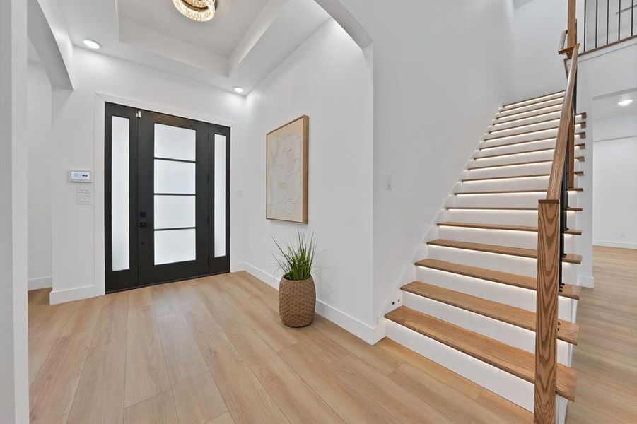 Entryway featuring wood-finish flooring, a contemporary front door with frosted glass panels, and a staircase with illuminated risers