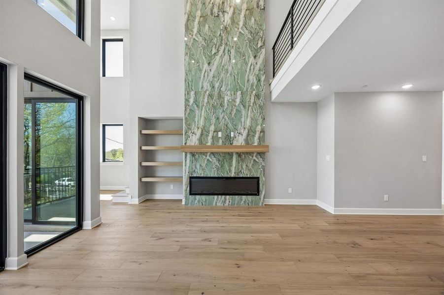 Unfurnished living room with a high ceiling, a large fireplace, light wood finished floors, plenty of natural light, and recessed lighting Unfurnished living room with a high ceiling, a large fireplace, light wood finished floors, plenty of natural light, and recessed lighting