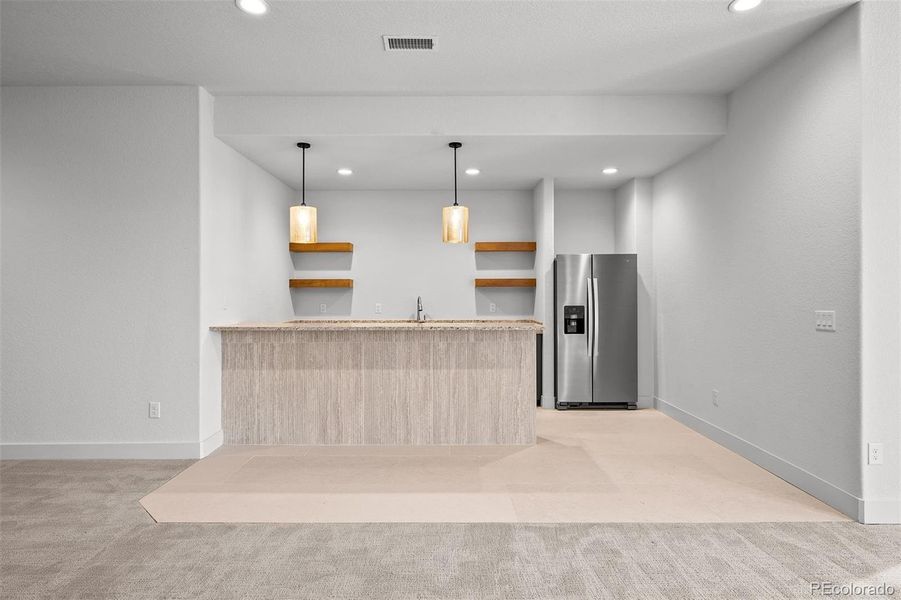 Wet bar with Himalayan Moon Caesarstone countertops, full-size refrigerator, slab flooring, and open shelving.