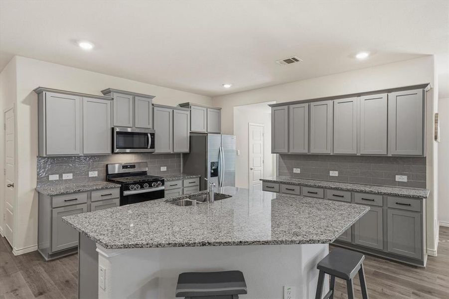 Kitchen with gray cabinets, a kitchen breakfast bar, stainless steel appliances, light wood-style floors, and recessed lighting Kitchen with gray cabinets, a kitchen breakfast bar, stainless steel appliances, light wood-style floors, and recessed lighting