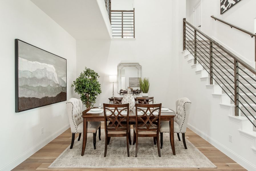 Formal dining room with wood table, tufted chairs, two-story ceiling, and staircase with metal railing