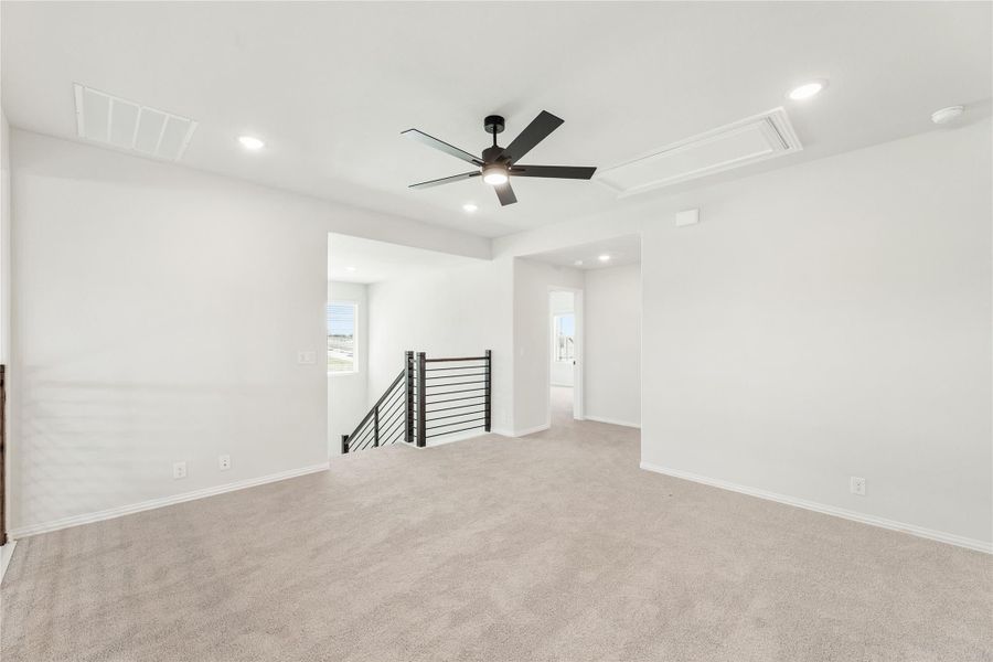 Spacious upstairs loft with carpet, ceiling fan, and open metal stair railing