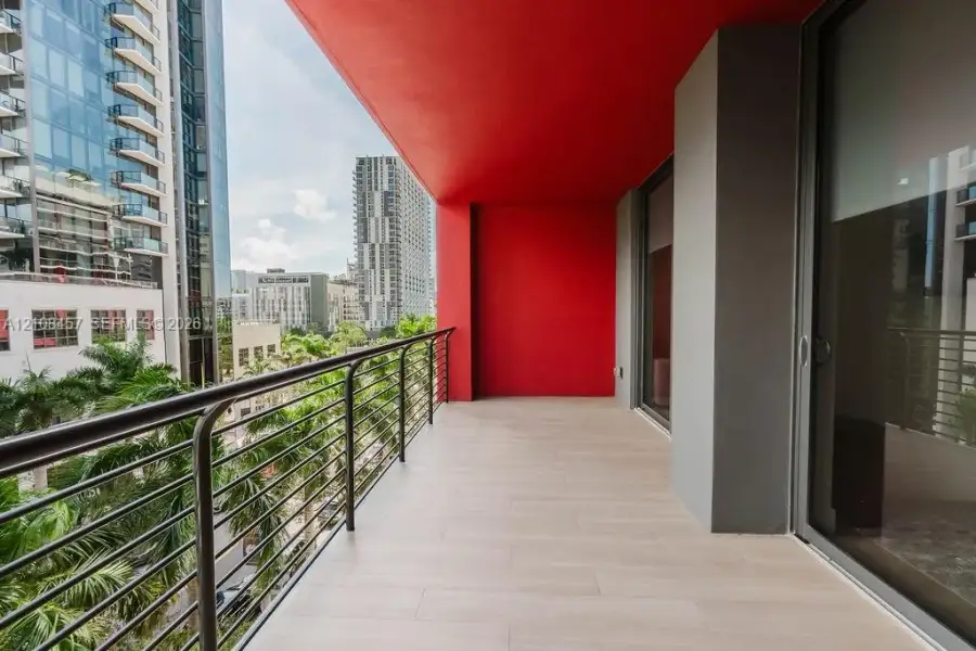 Covered balcony featuring wood-finish tile flooring, metal railing, and high-contrast red ceiling accent Covered balcony featuring wood-finish tile flooring, metal railing, and high-contrast red ceiling accent