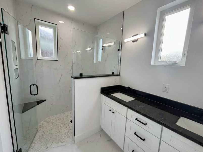 Bathroom with a marble finish shower, double vanity, and light marble finish flooring