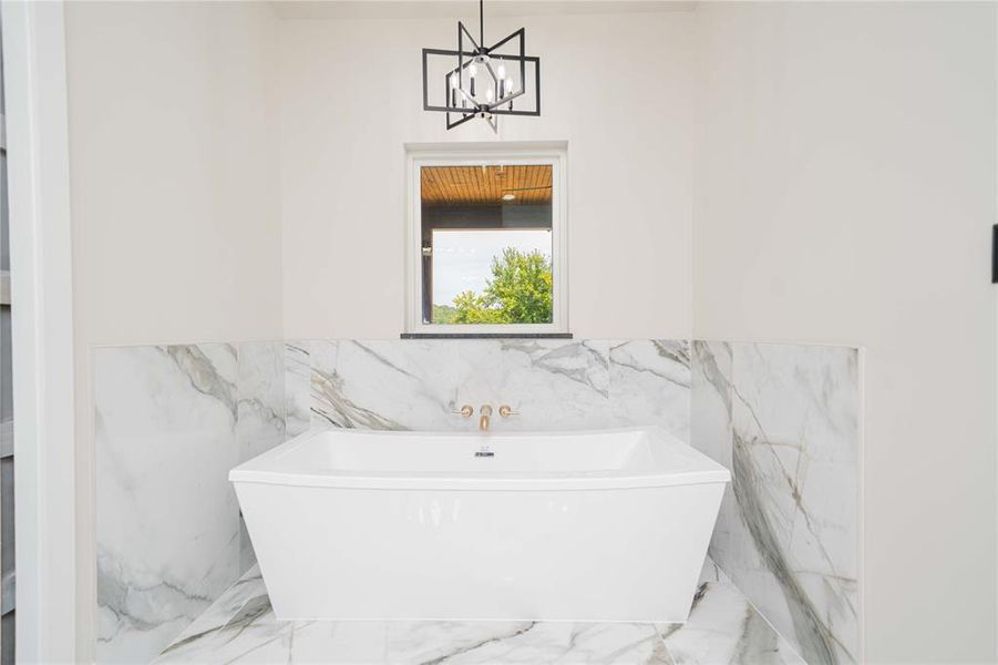 Freestanding soaking tub with gold-finish fixtures set against a white and gray veined tile surround