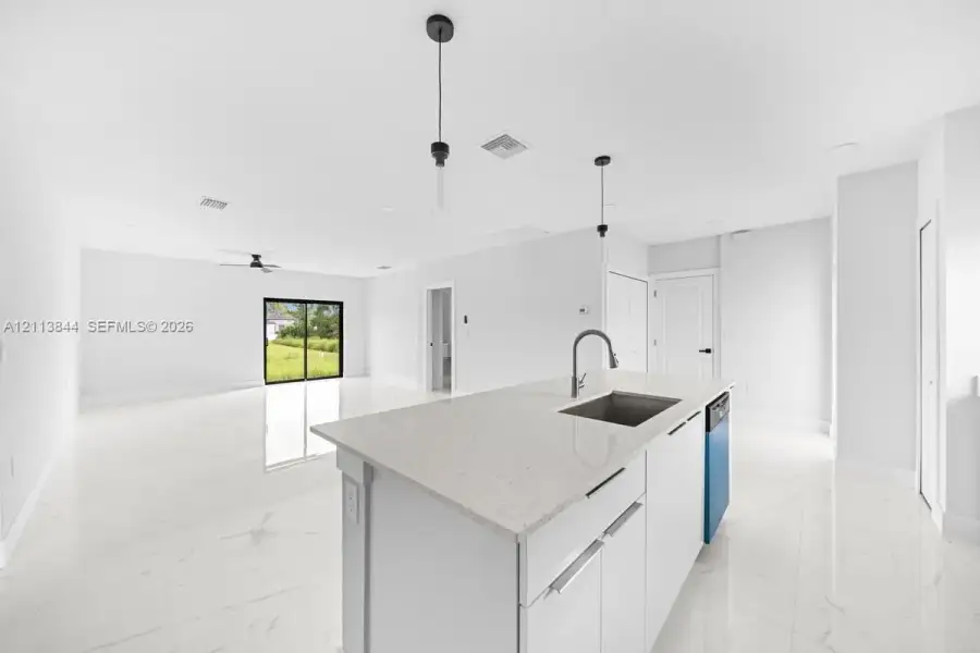 Kitchen island featuring a stone-composite countertop, undermount stainless steel sink, and sleek hardware, complemented by light-toned large-format tile flooring and minimalist pendant lighting Kitchen island featuring a stone-composite countertop, undermount stainless steel sink, and sleek hardware, complemented by light-toned large-format tile flooring and minimalist pendant lighting
