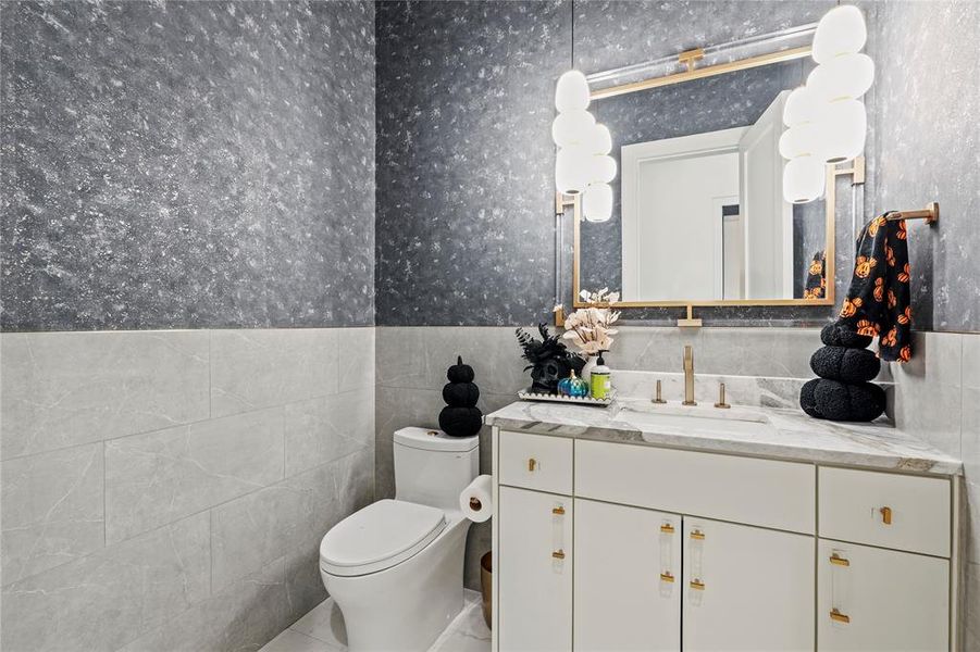 Half bath featuring tile walls, vanity, a wainscoted wall, and wallpapered walls Half bath featuring tile walls, vanity, a wainscoted wall, and wallpapered walls
