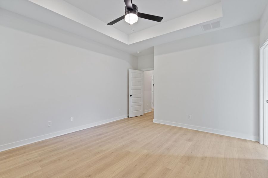 Tray ceiling with recessed lighting, wood-finish flooring, and a ceiling fan with integrated lighting