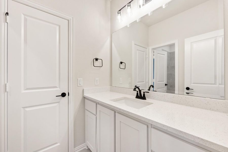 Bathroom vanity with white cabinets, quartz countertop, single sink, black fixtures, and large mirror with overhead lighting. Bathroom vanity with white cabinets, quartz countertop, single sink, black fixtures, and large mirror with overhead lighting.