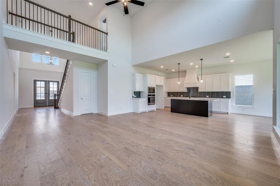 Unfurnished living room with a high ceiling, sink, light wood-type flooring, and ceiling fan