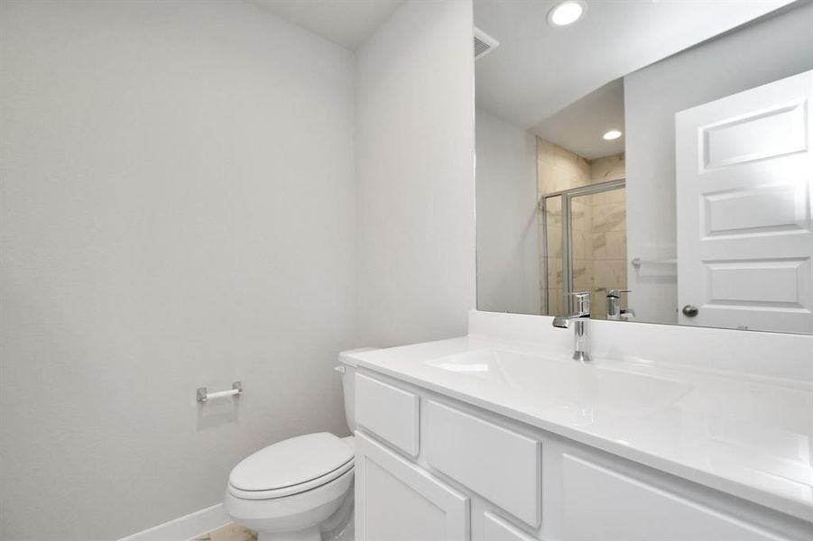 Experience sophistication in the guest suite bathroom, where tile flooring complements a walk-in shower with tile surround. Wood cabinets complete with a beautiful light countertop, enhances the space for a truly inviting ambiance. Sample photo of completed home with similar floor plan. As-built interior colors and selections may vary.