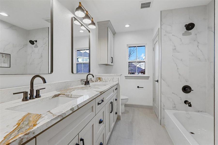 Full bathroom with vanity, tiled shower / bath, plenty of natural light, and toilet