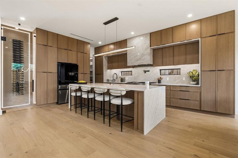 Gourmet kitchen featuring a large center island with integrated seating, built-in wine storage, extensive wood-finish cabinetry, integrated appliances, and light wood-finish flooring