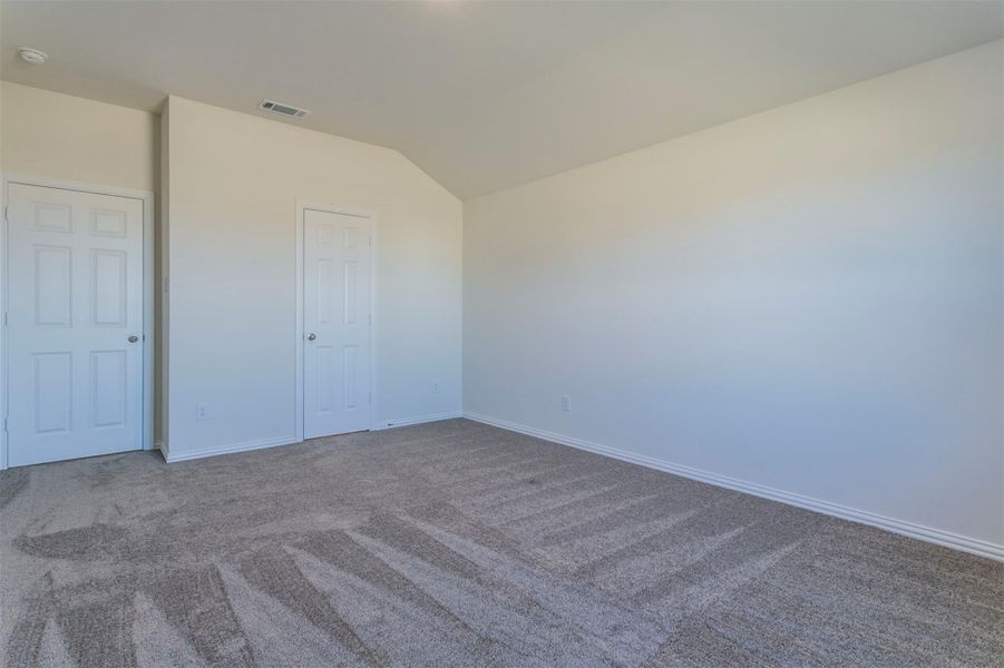 Unfurnished bedroom featuring baseboards, vaulted ceiling, visible vents, and carpet
