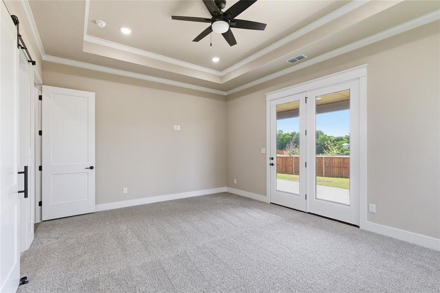 Spacious room featuring light gray carpet flooring, tray ceiling with recessed lighting, and a ceiling fan