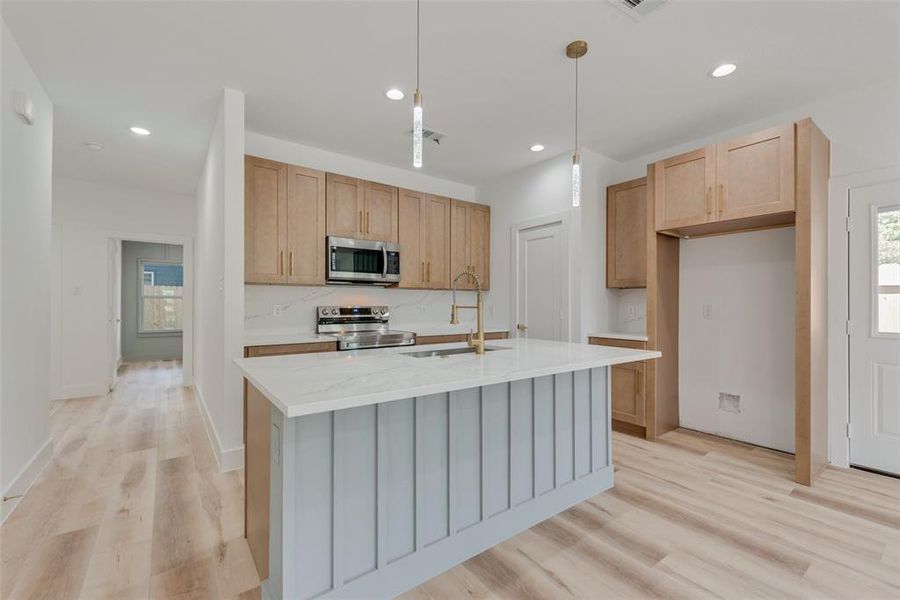 Kitchen with backsplash, sink, appliances with stainless steel finishes, light hardwood / wood-style flooring, and a center island with sink