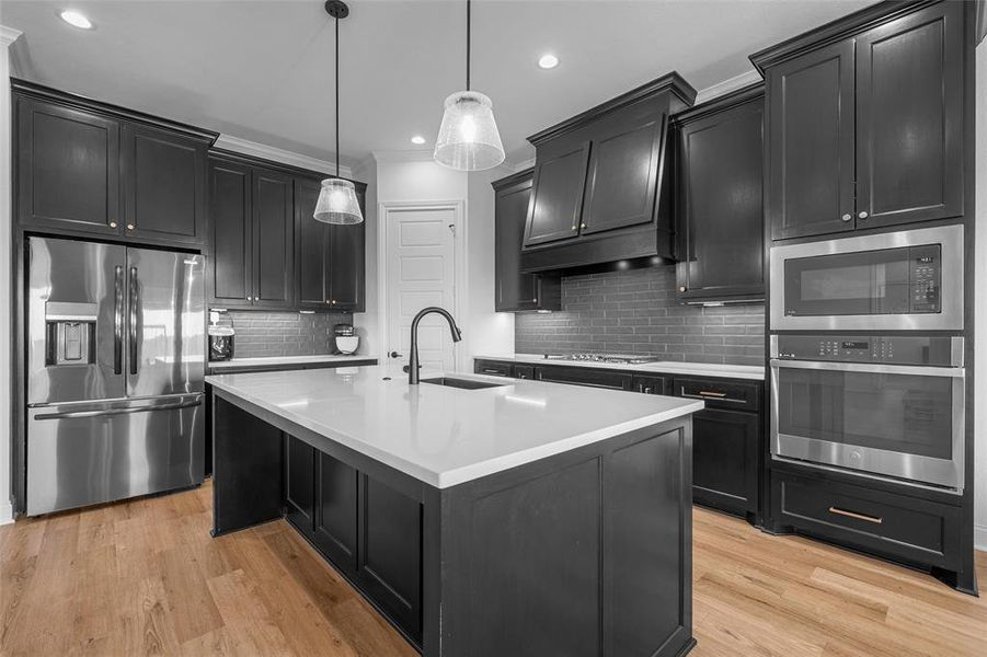 Kitchen featuring dark cabinets, stainless steel appliances, backsplash, light wood-type flooring, and a center island with sink Kitchen featuring dark cabinets, stainless steel appliances, backsplash, light wood-type flooring, and a center island with sink