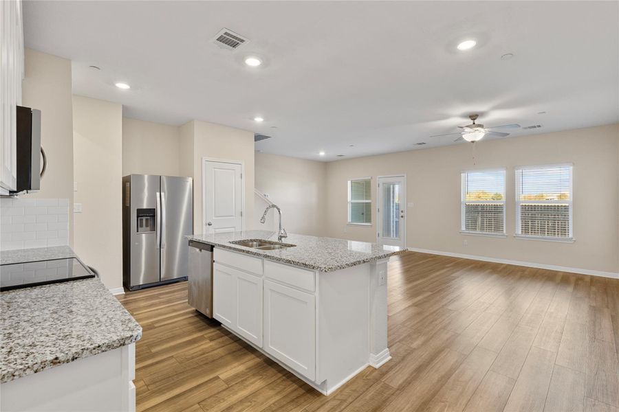 Kitchen/Living View featuring stainless steel appliances, light stone countertops, open floor plan, backsplash, and a center island with sink Kitchen/Living View featuring stainless steel appliances, light stone countertops, open floor plan, backsplash, and a center island with sink