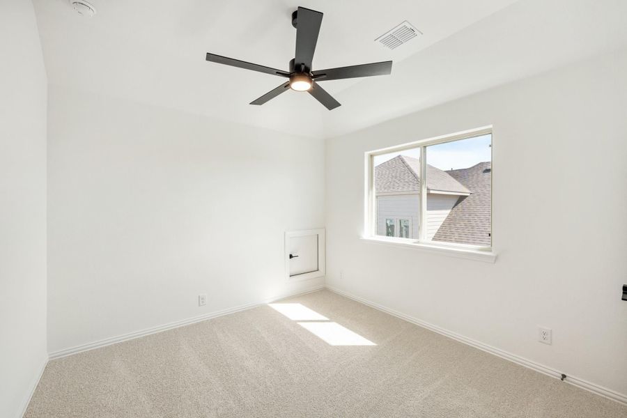 Empty bedroom with white walls, beige carpet, black ceiling fan, and a single window