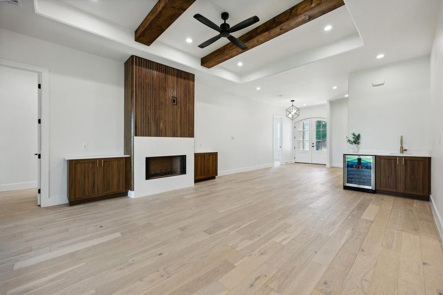 Unfurnished living room featuring ceiling fan, sink, beam ceiling, wine cooler, and light hardwood / wood-style flooring