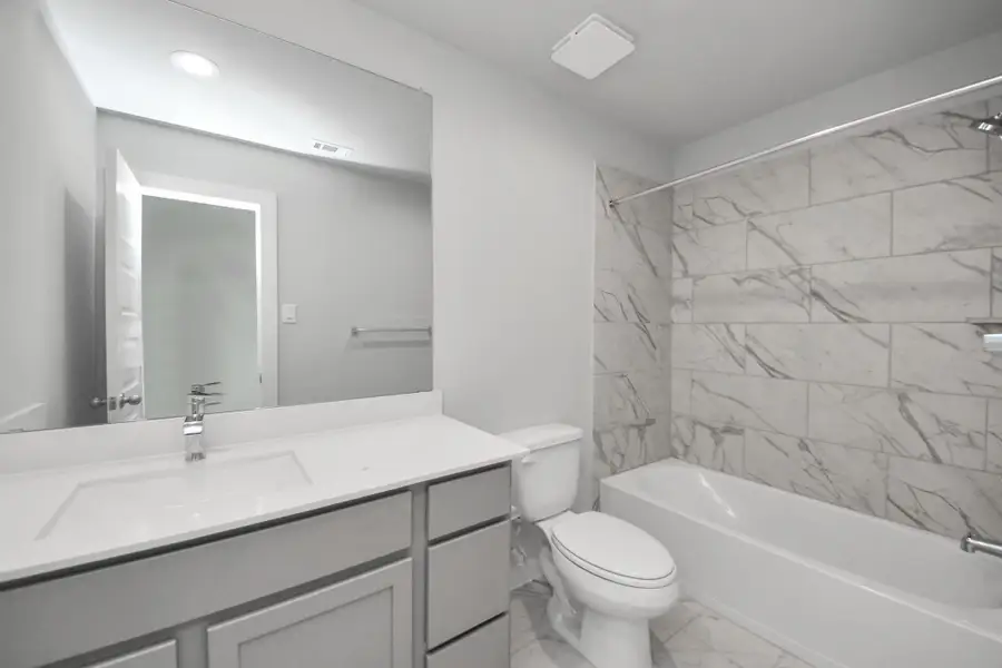 Secondary bath features tile flooring, bath/shower combo with tile surround, light stained wood cabinets, beautiful light countertop. Sample photo of completed home with similar floor plan. Actual colors and selections may vary.