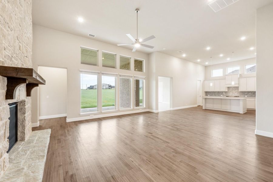 Open living room with stone fireplace, hardwood floors, high ceilings, and open kitchen in background