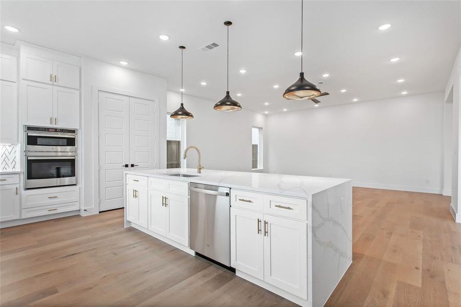 Kitchen with a kitchen island with sink, light hardwood / wood-style flooring, stainless steel appliances, and white cabinetry