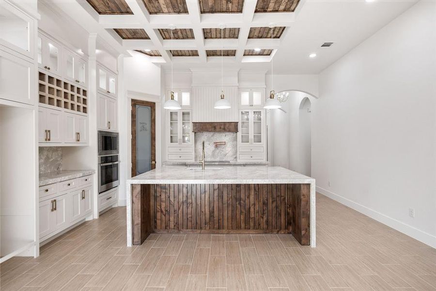 Kitchen featuring coffered ceiling, backsplash, glass insert cabinets, arched walkways, and beam ceiling