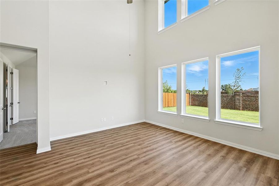 Unfurnished room featuring wood finished floors, a towering ceiling, and a ceiling fan Unfurnished room featuring wood finished floors, a towering ceiling, and a ceiling fan