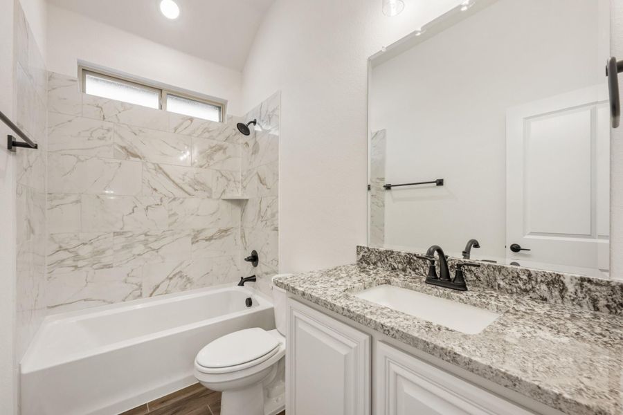 Bathroom with marble-tiled tub surround, granite vanity countertop, white cabinets, and black fixtures Bathroom with marble-tiled tub surround, granite vanity countertop, white cabinets, and black fixtures