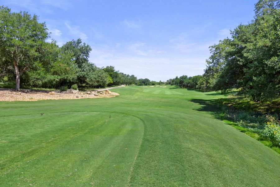 A well-maintained golf course awaits, nestled amongst mature trees under a clear sky.