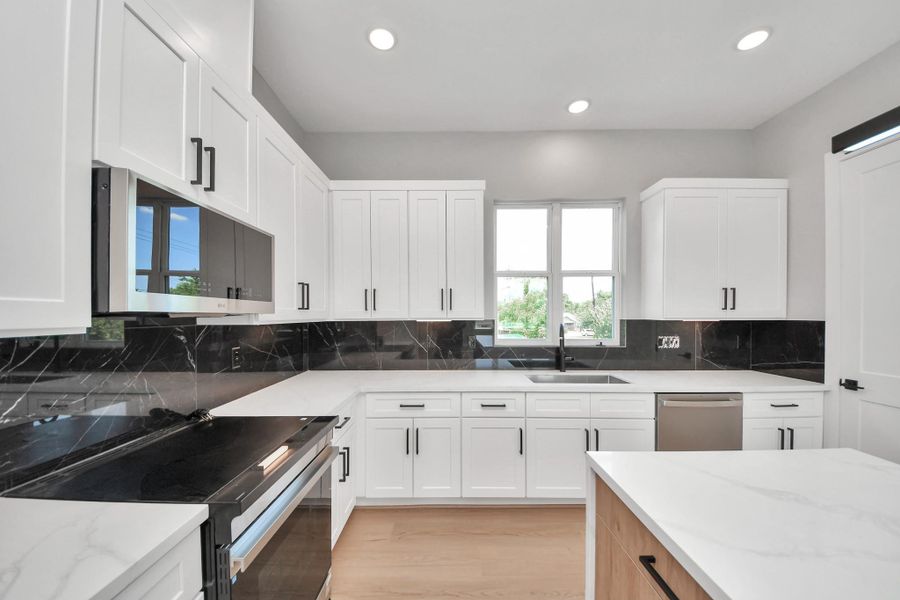 Designer kitchen featuring sleek quartz countertops, custom cabinetry, modern black accents, & a spacious waterfall island perfect for entertaining.