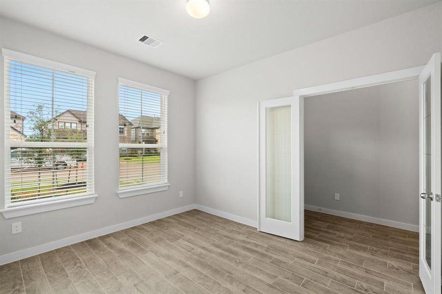 At the forefront, a refined home office beckons productivity and focus. Luxurious details like wood-look tile flooring, custom paint, expansive windows with privacy blinds, and French doors create an inspiring workspace. Sample photo of completed home with similar floor plan. As-built interior colors and selections may vary.