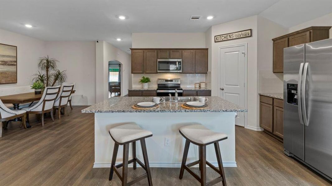 Kitchen featuring stainless steel appliances, dark wood finished floors, a kitchen island with sink, light stone counters, and tasteful backsplash