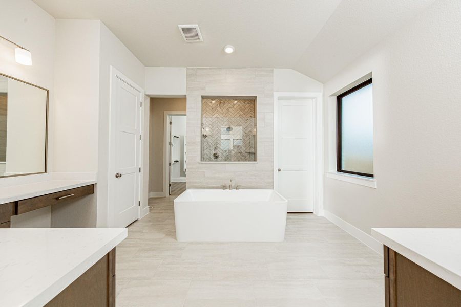 This elegant primary bathroom features a stylish dual-vanity layout with stained wood cabinetry, sleek brushed nickel fixtures, and clean-lined framed mirrors. Bright quartz countertops and modern lighting create a fresh, upscale feel, while the space opens seamlessly to the primary suite beyond, enhancing both flow and functionality.