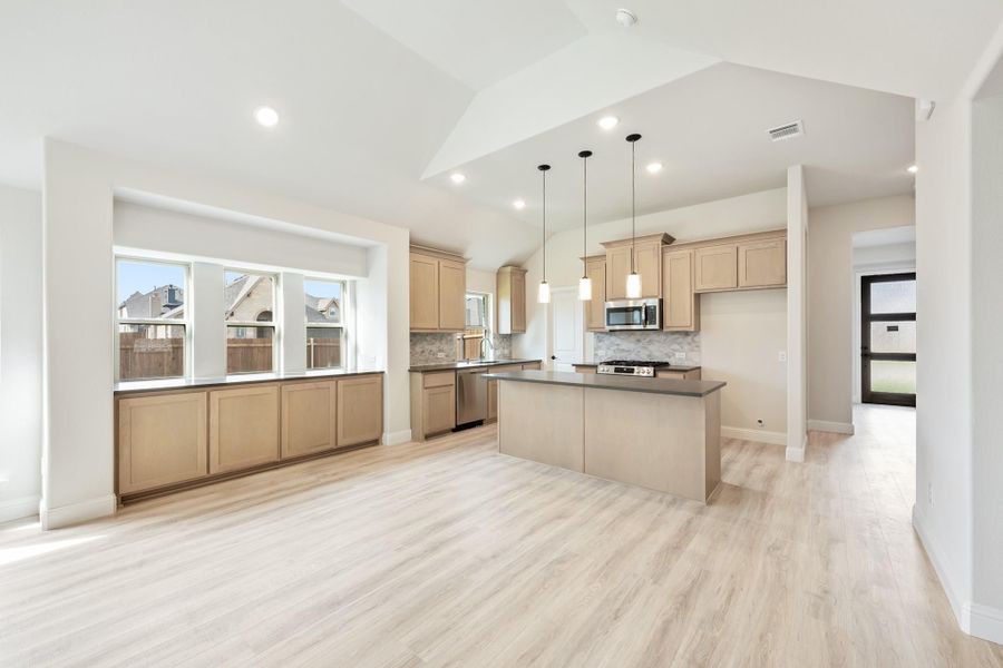 Open kitchen with tan cabinets, center island, pendant lights, and light wood floors