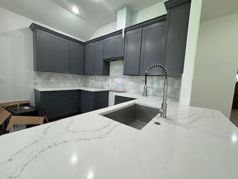 This kitchen features sleek dark cabinetry, marble-like countertops, and a modern backsplash, complete with a large undermount sink and contemporary faucet.