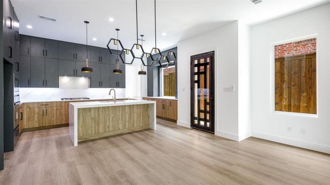 Kitchen featuring sink, an island with sink, pendant lighting, and light wood-type flooring