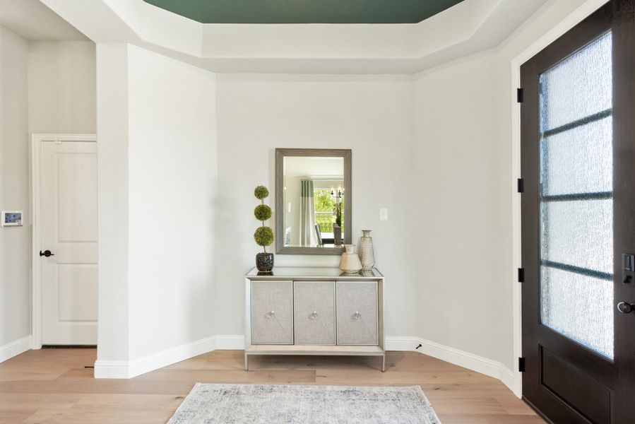 Foyer with dark front door, tray ceiling, console table, and hardwood floors