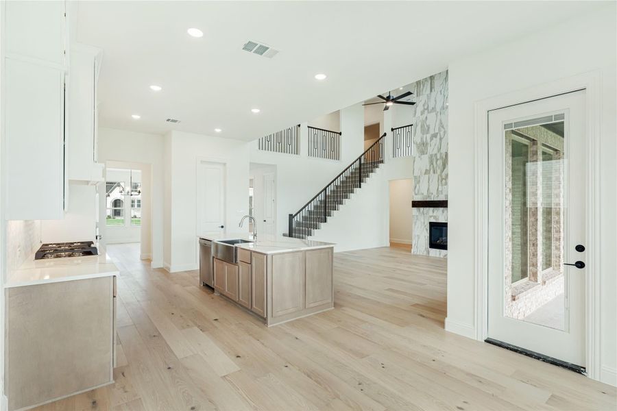 Open-concept kitchen with center island, light wood floors, and staircase leading to second floor balcony