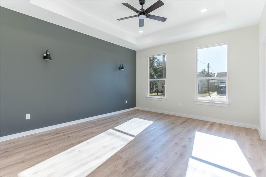 Unfurnished room featuring a raised ceiling, light wood-type flooring, recessed lighting, and a ceiling fan