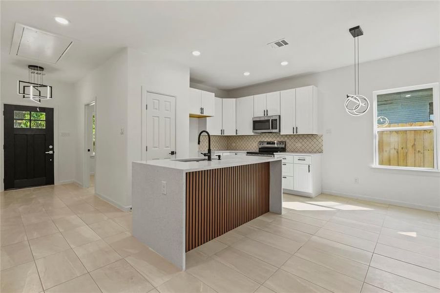 Kitchen with light tile patterned flooring, decorative backsplash, white cabinets, a center island with sink, and recessed lighting