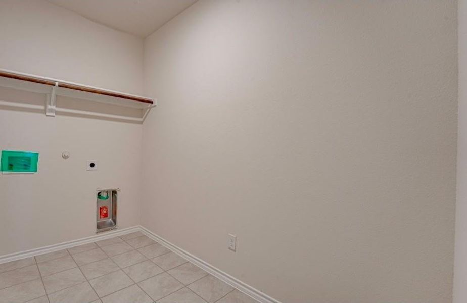 Utility area featuring neutral tile flooring, a wall-mounted shelving unit, and appliance hookups Utility area featuring neutral tile flooring, a wall-mounted shelving unit, and appliance hookups